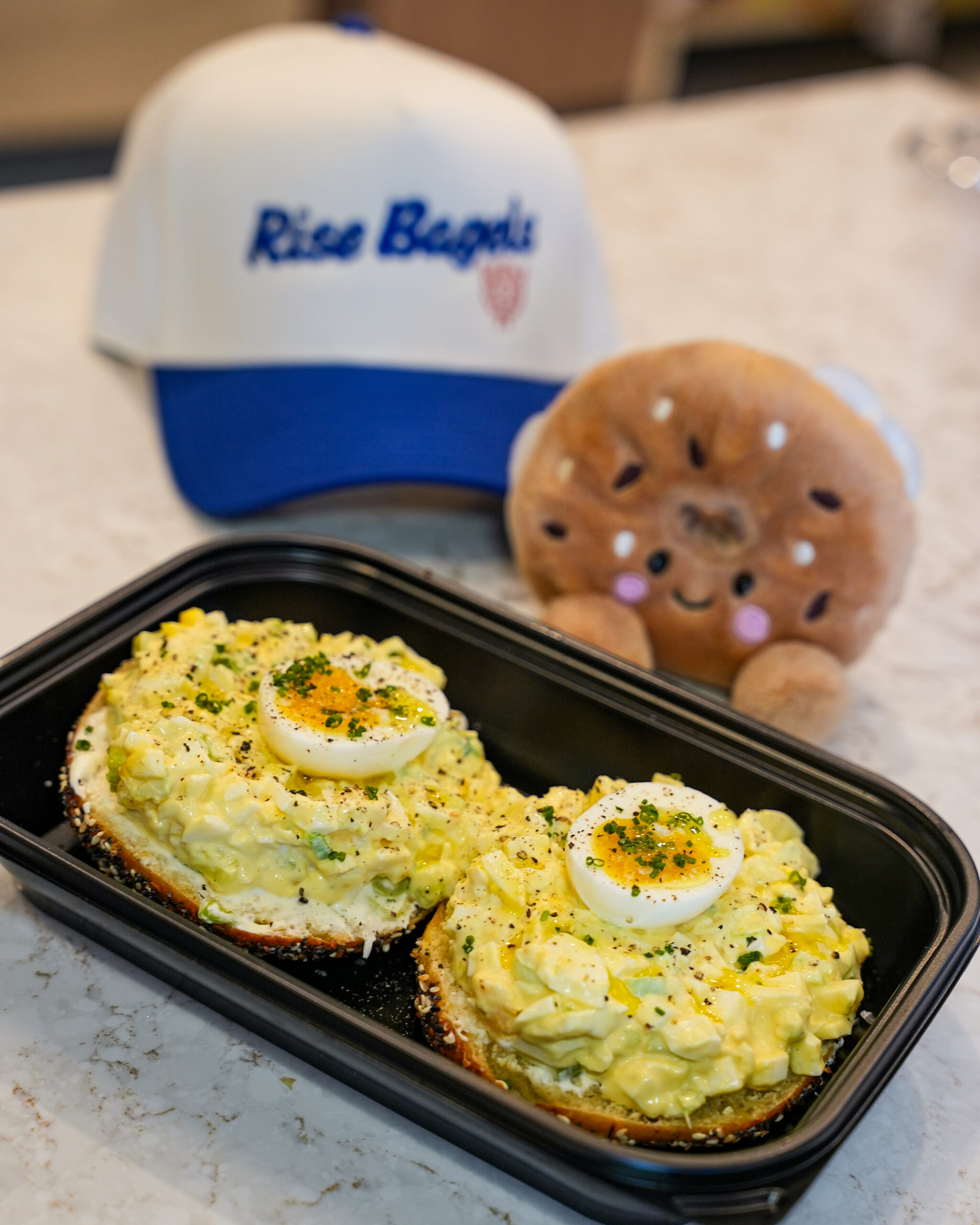 7-11 Tokyo bagel from Rise Bagels which consist of eggs and a bagel plushie and Rise Bagels cap in the background