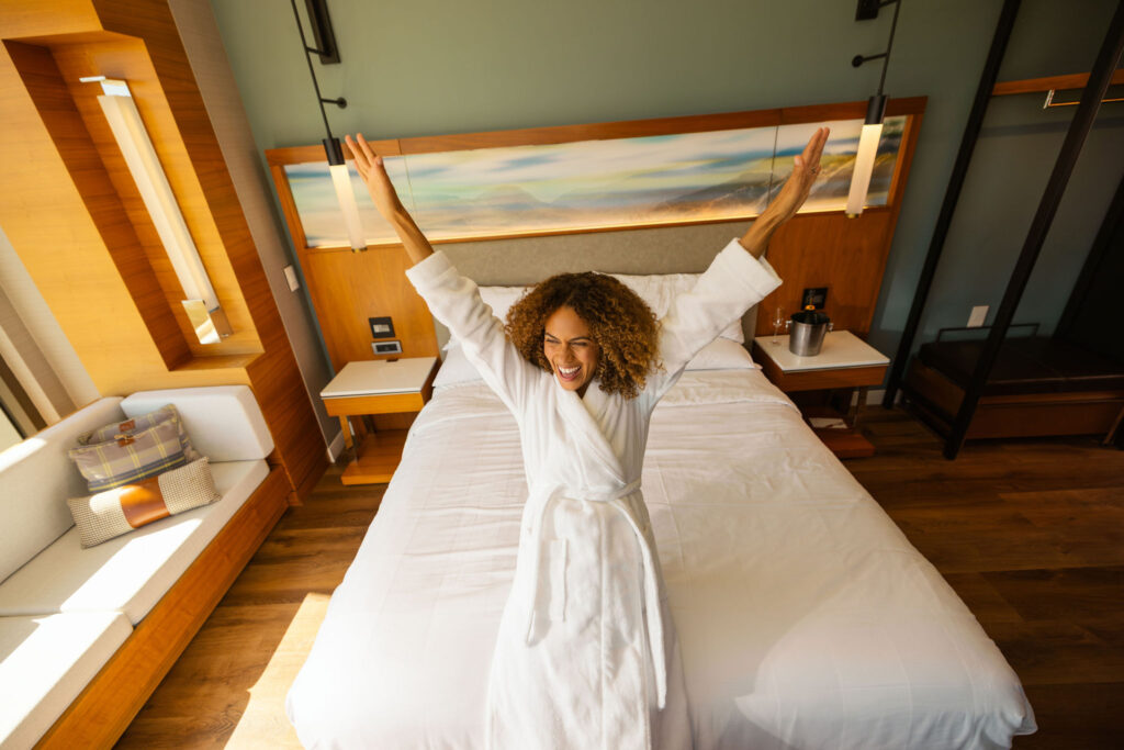 woman in white bathrobe about to lie down on the bed at Marriott Irvine Spectrum hotel