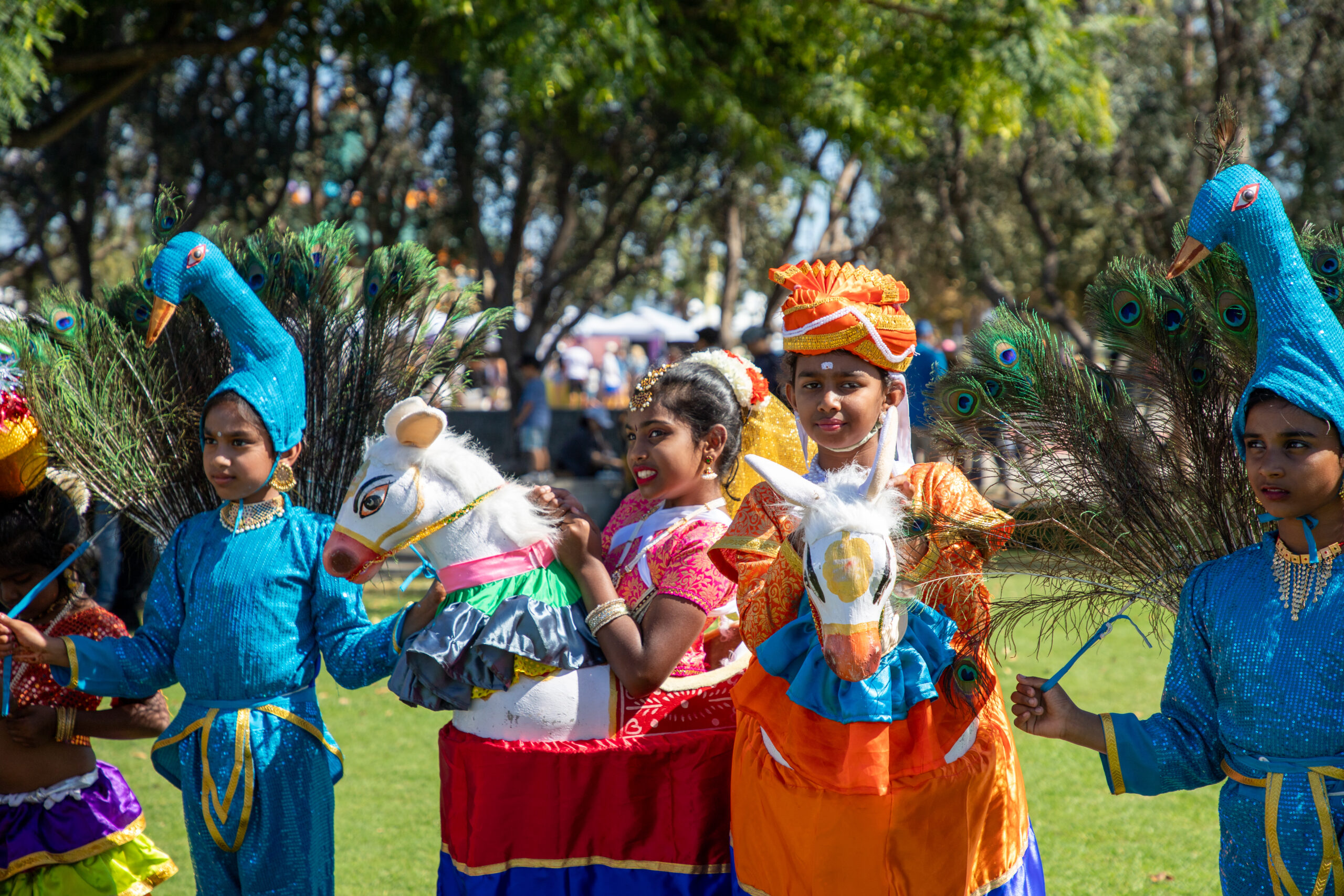Four children outdoors on a sunny day in animal costumes with two dressed as a peacock and the other two as a horse